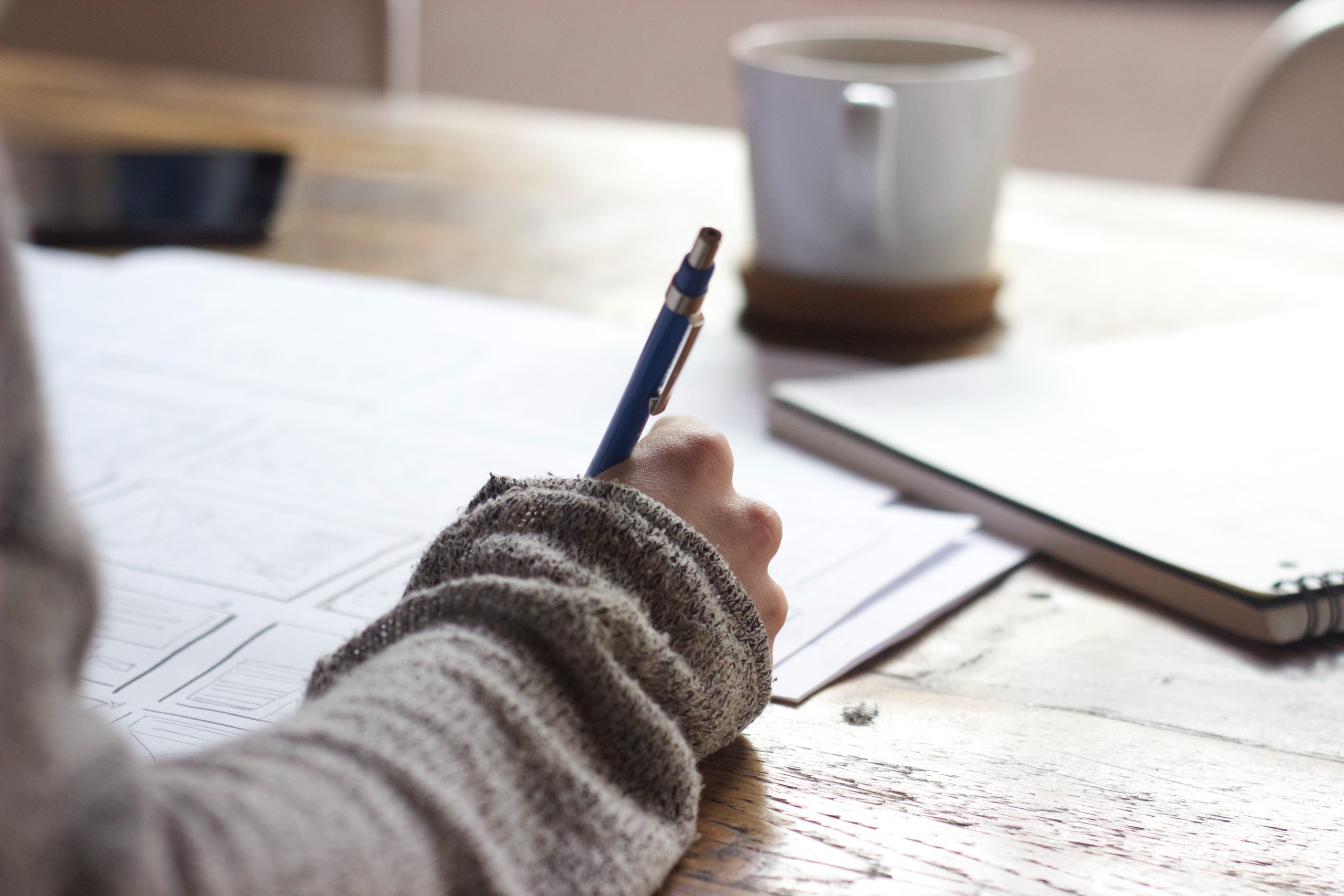 Student writing at desk with mug